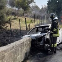 Automobile incidentata accanto al muretto; pompiere indiviso di fronte, fiamme spente, scena di soccorso stradale in area rurale.