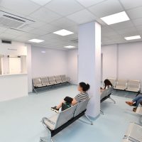 Sala d'attesa moderna con sedie metalliche e colonne, illuminazione soffusa e visitatori seduti in attesa.
