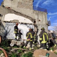 Vigili del fuoco in azione davanti a un edificio parzialmente crollato, attrezzature e fiamme spezzate, in un contesto urbano