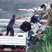 Gruppo di persone su una passerella vicino all’acqua, con alcuni in piedi e altri seduti, in un contesto all’aperto.