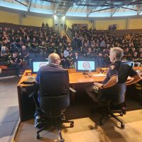 Aula conferenze con pubblico numeroso, tre relatori seduti sul palco di fronte a una platea attenta in un auditorium.