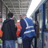 Operai e tecnici su una banchina di stazione, indossano giubbotti ad alta visibilità vicino a un treno in attesa di lavoro.