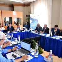 Riunione formale tra professionisti seduti attorno a una tavola rotonda, discussione di lavoro e presentazioni, ambiente aziendale.