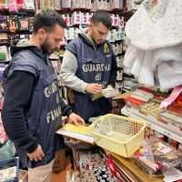 Due agenti delle forze dell’ordine ispezionano una libreria/negozio di carte, osservando manuali e documenti su scaffali e bancone in ambiente interno.