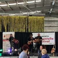 Pubblico che assiste a una band sul palco in un festival all’aperto, con decorazioni e scritte sullo sfondo.
