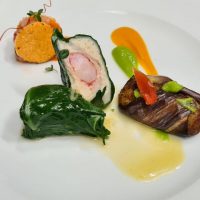 Antipasto elegante: involtino di carne con ortaggio, purea di zucca, verdure glassate e salsa leggera su piatto bianco