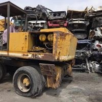 Carroponte giallo arrugginito in un deposito-industriale con cumuli di scarti metallici sullo sfondo.
