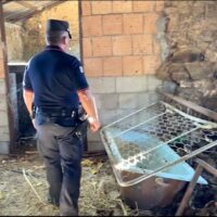 Poliziotto in uniforme esamina una scena in un edificio demolito, con strutture in mattoni e attrezzature metalliche circostanti.