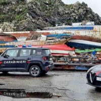 Barche rovesciate e autoscafi, camionetta dei Carabinieri in primo piano su fondo di banchina e rocce: scena di un incidente nautico.
