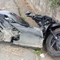 Moto sportiva danneggiata su strada, parabrezza assente e telaio graffiato, sedile nero e ruote spazzolate.
