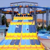 Scivolo d'acqua multicolore in giallo e azzurro con sedili e percorsi, parco divertimenti all'aperto.