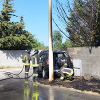 Immagine di vigili del fuoco all'opera, soccorso incendio stradale vicino a muretto, con fumo e strumenti, in pellegrino ambiente urbano.