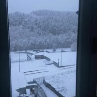 Scorcio invernale visibile da una finestra: colline innevate, tetti e cortili coperti di neve, atmosfera tranquilla e fredda.