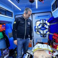 Medico in jeepare a bordo di un’ambulanza, controlla l equipment sanitario su una barella, interno blu e luci neon.