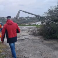 Gruppo di persone in abiti colorati si avvicina a un’area di cantiere con una pipa di cemento rotta e logorato; terreno fangoso e alberi sullo sfondo.