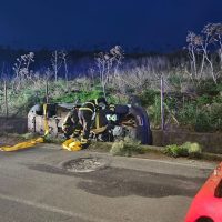 Soccorritori al lavoro accanto a un incidente stradale durante la notte, con attrezzature e una lastra gialla sul bordo della carreggiata.