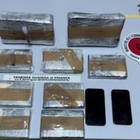 Sequestro di droga su tavola: panetti di droga avvolti in plastica, etichette e telefoni scuri sullo sfondo.