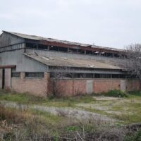 Fabbrica abbandonata in rovina: muri di mattoni, tetto crollato e un terreno erboso deserto intorno, atmosfera malinconica.