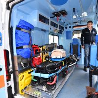 Interno di un’ambulanza: lettiga, cassette medico, túrbine e attrezzature pronte, soccorritore in piedi accanto all’ambulanza