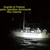 Barca in notturna con figure sul ponte; testo giallo: Guardia di Finanza, reparto Operativo Aeronavale Vibo Valentia, a sinistra in alto.