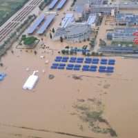 Veduta aerea di una spiaggia affollata con lettini blu allineati, ombrelloni, strutture alberghiere e aree giochi, sabbia ampia e mare sullo sfondo.