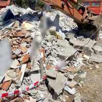 Cantiere con detriti: blocchi di cemento, ferri e detriti vari sparsi, appesi a una zona di demolizione all’aperto.