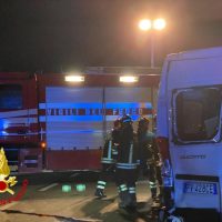 Ambulanza e vigili del fuoco al lavoro di notte, personale in abiti protettivi vicino al mezzo di soccorso illuminato da fari.