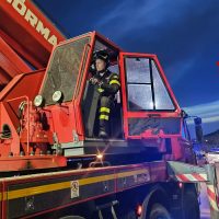 Operatore in casco e tuta fluorescente su piattaforma di gru rossa, cielo blu, scena di cantiere o soccorso tecnico.