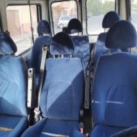Interni di un pullman con sedili blu, separatori e finestrini, atmosfera ordinata e luminosa.