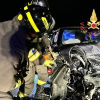 Soccorritori all’opera tra le lamiere contorte dell’auto coinvolta in incidente, illuminata da fari e casco a visiera.