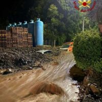 Cantiere lungo una strada di campagna con pozza d'acqua fangosa, pallets e serbatoi, in una giornata umida.