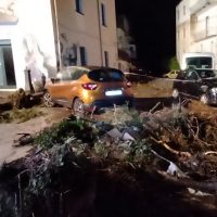 Auto giallo parcheggiata vicino a una casa di notte, strade piene di rami e detriti derivanti da un albero abbattuto.