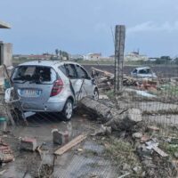 Auto danneggiata tra rottami e palizzate su terreno fangoso, scenario di incidentata zona urbana in demolizione.