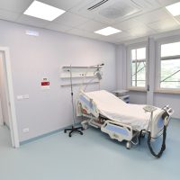 Sala d’ospedale: degenza con letto medico a colonne, monitor e attrezzature, finestra e luci fluorescenti, pavimento azzurro chiaro.