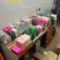 Scorri bi chiaro: mazzette di banconote colorate e pacchetti in ordine su tavolo in una stanza; scena di denaro contante stoccato e codici colori.