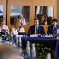 Gruppo di professionisti in una conferenza, discussione tra relatori al tavolo principale in ambiente formale.