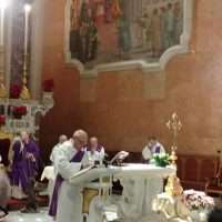 Celebrazione religiosa in chiesa: sacerdote e chierici all’altare durante una messa, con arredamento sacro e architettura antica sullo sfondo.