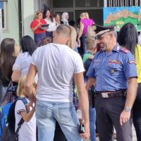 Gruppo di persone all’aperto coinvolte in un evento, con agenti in uniforme e pubblico sullo sfondo.