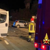 Incidente stradale notturno: autovetture e veicoli di soccorso presenti su strada, vigili del fuoco in azione.