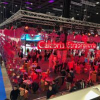 Stand esposizione colorato con luci rosse, persone che socializzano e tavoli: scena vivace di un evento fieristico a, Calabria Strabordiane.