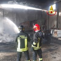 Due pompieri in divisa piena, spezzano un incendio in una struttura bruciata, vapore e fumo nell’aria, luci di emergenza e attrezzature attorno.