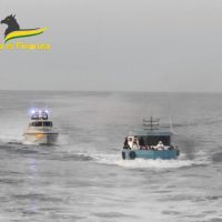 Due gommoni in mare aperto avvicinati tra loro, scia e acqua frastagliata, cielo grigio e luce fioca.