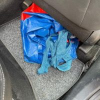 Borsa e abiti colorati lasciati sul sedile posteriore di un’auto, tessuti svolazzanti su tessuto grigio.