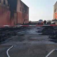 Effetto incendio su strada asfaltata tra edifici, contatori d'acqua e catene di accesso; atmosfera di cantiere e contesto urbano.