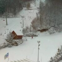 Ritratto dall'alto di una stazione sciistica invernale: neve copre piste, alberi e una piccola baita rossa.
