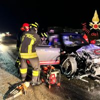 Intervento di soccorso stradale di notte: vigili e soccorritori accanto a due veicoli incidentati, lampeggianti e traffic control visibile.