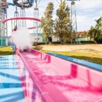 Bambino scivola su una rampa rossa in un parco acquatico soleggiato, tra spruzzi d'acqua e colori vivaci.