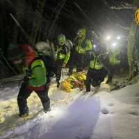 Escursionisti in giacca ad alta visibilità soccorso in valanga: squadra al lavoro in terreno innevato notturno, luci accese.