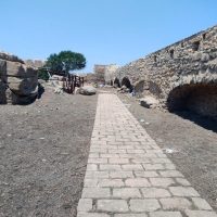 Cartina di pietra in una strada lastricata tra rovine e mura antiche, con cielo azzurro e paesaggio arido.