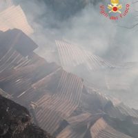 Catastrofe: tetti in fiamme tra fumo denso e macerie, atmosfera caotica e rossa di spegnimenti.